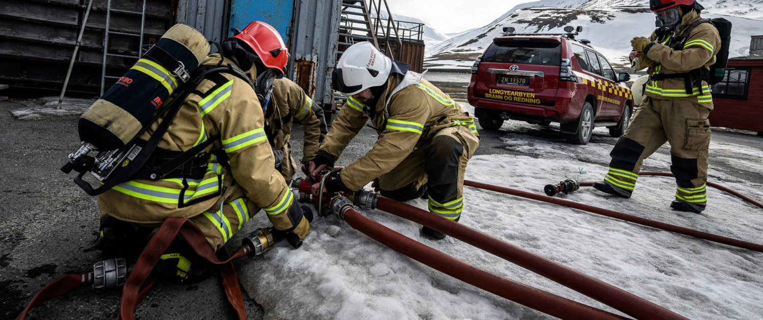 Brannvesen på redningsoppdrag på Svalbard. Tre personer kobler sammen slanger.